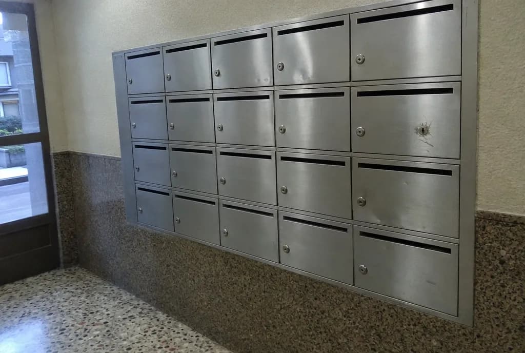Bloque de buzones metálicos empotrado en la pared del portal de un edificio de viviendas, con una de las cerraduras dañada