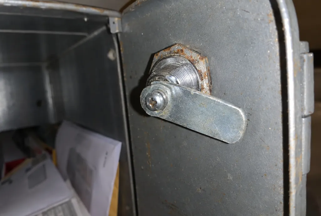 Cara interior de la puerta de un buzón metálico con la tuerca hexagonal y la leva atornillada al final del cilindro